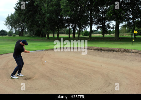 Maschio adulto golfista prendendo un bunker shot con la sfera nella sabbia Foto Stock