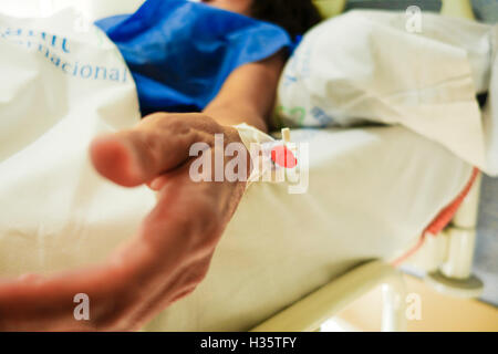 Stretta di mano di donna getting connected a IV, terapia endovenosa in ospedale. Foto Stock