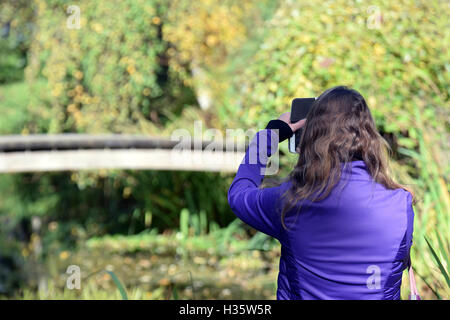 Donna di scattare una foto al parco con il suo smart phone. Foto Stock