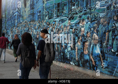 NYC pedoni a piedi passato un grande murale dipinto da Logan Hicks sulla Bowery parete murale, Houston Street Foto Stock