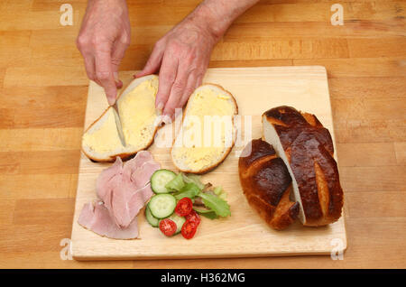 Coppia di mani buttering pane per un prosciutto sandwich insalata su un piano di lavoro di una cucina Foto Stock
