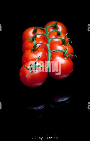 Grappolo di pomodori rossi su un nero sfondo riflettente Foto Stock