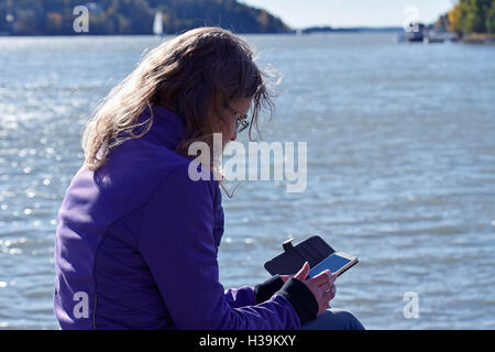 Donna che utilizza un telefono intelligente sulla spiaggia. Un bellissimo mare sullo sfondo. Foto Stock