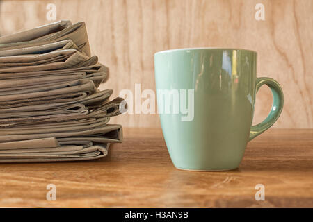 Tazza da caffè su di un tavolo di legno con una pila di quotidiani Foto Stock