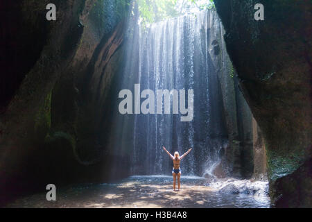 Donna felice traveler con i bracci sollevati per godersi la vita a una bella cascata nella foresta pluviale di Bali Foto Stock