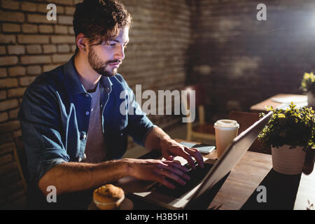 Giovane uomo concentrandosi su laptop mentre è seduto presso il cafe Foto Stock