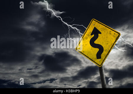 Winding Road Sign contro un sfondo tempestoso con lampi e copia di spazio. Sporco e cartello angolato aggiunge al dramma. Foto Stock