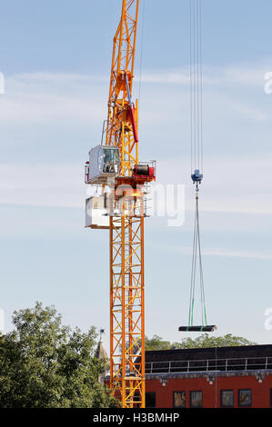 Piattaforma e cabina di una gru da cantiere con operatore il sollevamento di una pila di tubi in acciaio Foto Stock