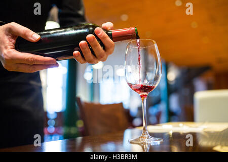 Cameriere versando il vino rosso in vetro Foto Stock