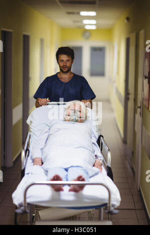 Ward boy spingendo un senior paziente sulla barella in corridoio Foto Stock