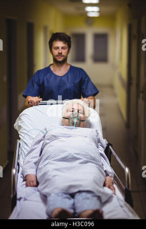 Ward boy spingendo un senior paziente sulla barella in corridoio Foto Stock