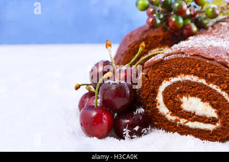 Natale Yule Log, Buche de Noel, torta al cioccolato con la diramazione, fresche Ciliege e festoso berry decorazioni su un bianco che serve p Foto Stock