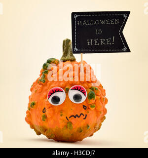 Primo piano di una zucca terrorizzata con una bandiera nera a forma di cartello con il testo di Halloween è qui scritto in essa, contro un off- Foto Stock