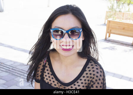 Donna che indossa gli occhiali da sole, sorridente allegramente, ritratto Foto Stock