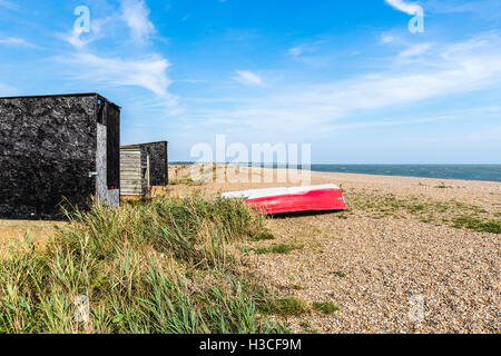 Rosso capovolta barca a remi sulla spiaggia sassosa a Dunwich, un villaggio nel Suffolk Coastal ergion, East Anglia, REGNO UNITO Foto Stock