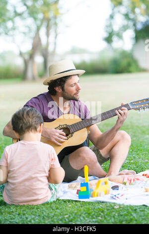 Padre suonare la chitarra acustica accanto al figlio Foto Stock