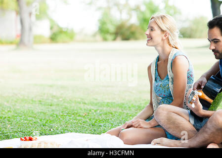Donna ascoltando uomo suonare la chitarra acustica mentre il pic-nic nel parco Foto Stock