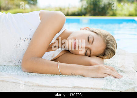 Donna in appoggio sul bordo della piscina con gli occhi chiusi Foto Stock
