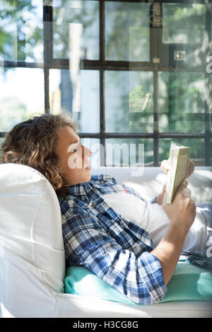 Giovane uomo leggendo un libro sul lettino Foto Stock