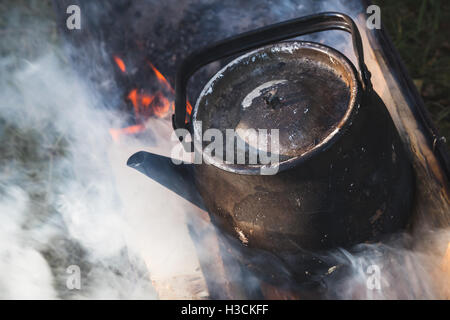 Vecchio usato il nero teiera con acqua bollente sorge su di un falò Foto Stock