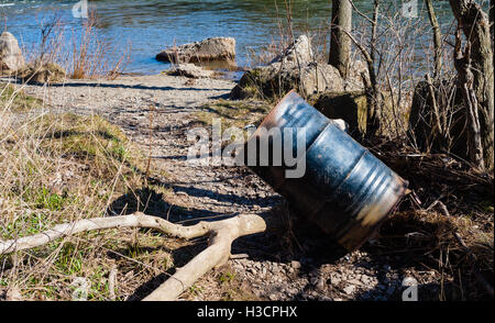 In parte in metallo arrugginito immondizia può o tamburo appoggiata sul ramo sul sentiero di ghiaia vicino al fiume. Foto Stock