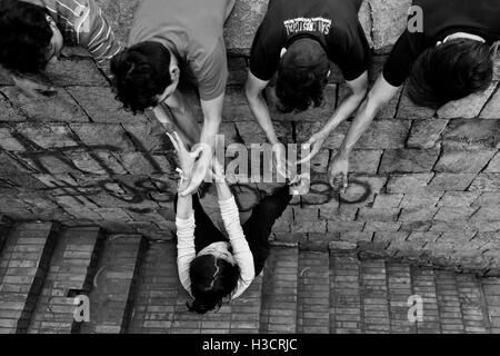 Un colombiano freerunner femmina, appeso su i suoi compagni' le mani, si arrampica sulla parete durante un allenamento parkour in Bogotá, Colombia. Foto Stock