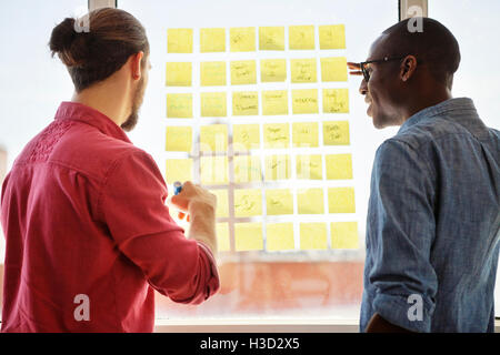 Vista posteriore di uomini di affari di discutere e scrivere note adesive Foto Stock