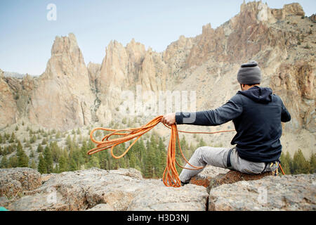 Vista posteriore del rocciatore gettando la corda mentre posa sulla montagna Foto Stock
