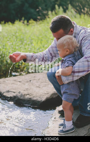 Baby boy guardando al padre la caduta di acqua in stagno Foto Stock