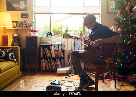 Uomo a suonare la chitarra mentre è seduto su una sedia a casa Foto Stock