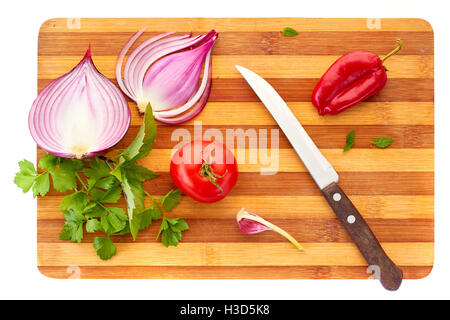 Cipolla rossa affettata, tomatoe, pepe, aglio, basilico e prezzemolo con coltello sulla tavola di legno su sfondo bianco. Foto Stock