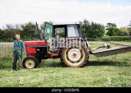Un fermo il trattore rosso e inclinazione pilota contro il cofano, in un campo in estate. Foto Stock