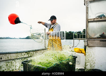 Un pescatore in piedi su una barca di gettare i galleggianti per la diffusione della rete sopra l'acqua. Foto Stock