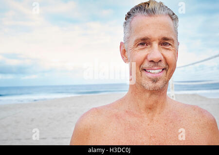 Uomo maturo in piedi su una spiaggia, sorridente alla fotocamera. Foto Stock