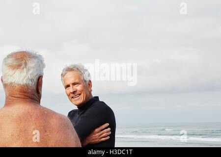 Due alti uomini in piedi su una spiaggia in chat, uno che indossa una muta. Foto Stock