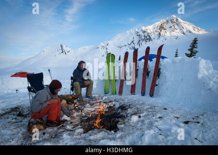 Gli appassionati di snowboard appendere fuori attorno a un fuoco durante il tramonto al campo base Foto Stock