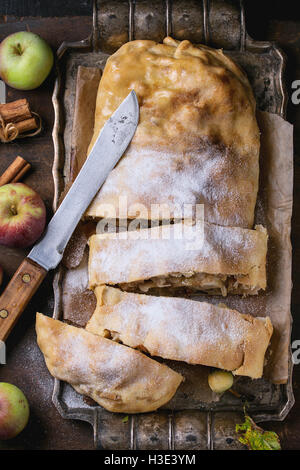 Affettato in casa lo strudel di mele servito con mele fresche con foglie, bastoncini di cannella e zucchero in polvere su vintage vassoio metallico con Foto Stock