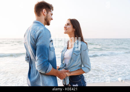 Felice coppia giovane in amore in piedi e tenendo le mani sulla spiaggia Foto Stock