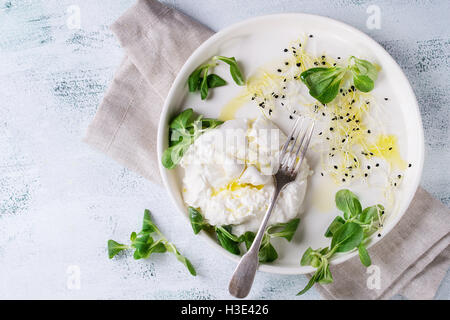 Fette di formaggio italiano burrata con forcella vintage, fresca insalata di mais, germogli di soia e olio di oliva in ceramica bianca sulla piastra napki tessili Foto Stock