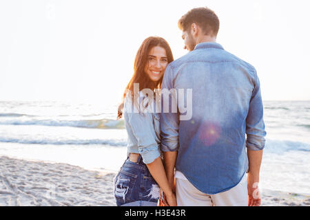 Giovane e bella donna che mantiene il suo fidanzato mano che in piedi indietro in spiaggia Foto Stock