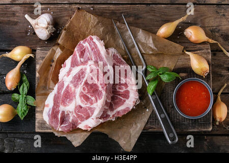 Materie bistecca di carne di maiale sul tagliere con scalogno cipolla, salsa di pomodoro per la marinata, basilico e condimento, servita con carni forcella Foto Stock