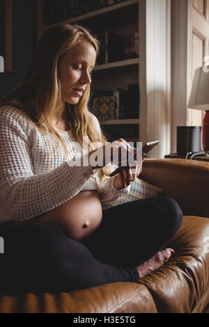 Donna incinta tramite telefono cellulare nel soggiorno Foto Stock