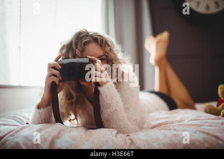 Donna facendo clic su foto da una fotocamera digitale in camera da letto Foto Stock