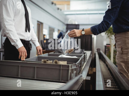 Il passeggero mettendo il sacchetto in plastica nel vassoio per il controllo di sicurezza Foto Stock