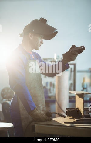 Saldatore maschio esaminando un pezzo di metallo Foto Stock