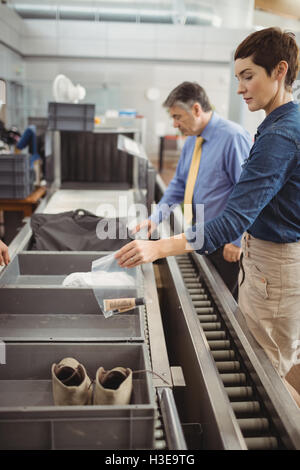 Il passeggero mettendo il sacchetto in plastica nel vassoio per il controllo di sicurezza Foto Stock