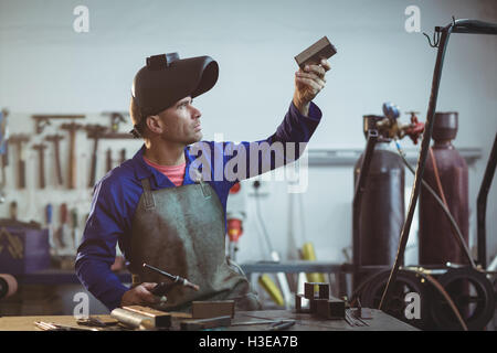 Saldatore maschio esaminando un pezzo di metallo Foto Stock