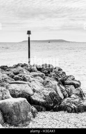 Immagine in bianco e nero di un post di avviso su un promontorio roccioso a Ringstead Bay, Dorset, Inghilterra, Regno Unito, Portland Bill in distanza Foto Stock