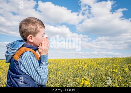 Little Boy in giallo canola field soffia il naso e che soffrono di allergia al polline. Foto Stock