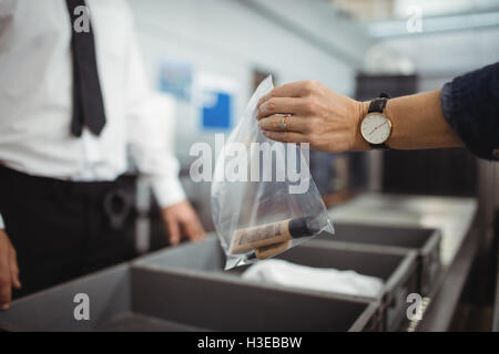 Il passeggero mettendo il sacchetto in plastica nel vassoio per il controllo di sicurezza Foto Stock